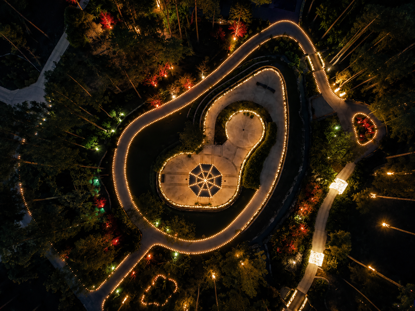 Aerial view of the Longview Arboretum illuminated with warm holiday lighting along winding paths and gardens.